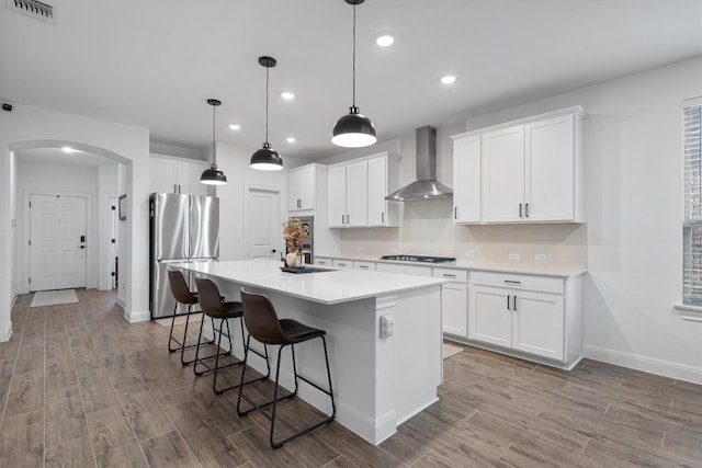 kitchen with wall chimney exhaust hood, white cabinetry, hanging light fixtures, and stainless steel refrigerator