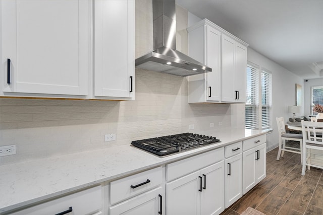 kitchen featuring white cabinetry, dark hardwood / wood-style floors, stainless steel gas cooktop, wall chimney exhaust hood, and light stone counters