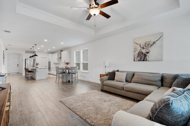 living room featuring crown molding, light wood-type flooring, and a raised ceiling