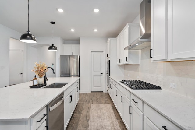 kitchen featuring white cabinets, appliances with stainless steel finishes, hardwood / wood-style flooring, a kitchen island with sink, and wall chimney exhaust hood