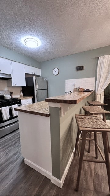 kitchen featuring dark hardwood / wood-style floors, extractor fan, stainless steel appliances, a breakfast bar, and white cabinetry