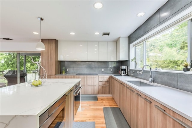 kitchen featuring white cabinets, sink, hanging light fixtures, built in microwave, and light stone counters