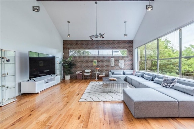 living room featuring high vaulted ceiling, light hardwood / wood-style floors, and brick wall