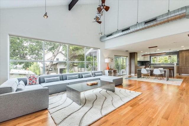 living room with light wood-type flooring, a towering ceiling, and beamed ceiling