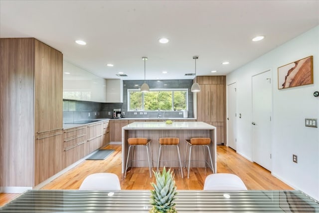 kitchen featuring white cabinets, hanging light fixtures, decorative backsplash, a kitchen island, and a kitchen bar