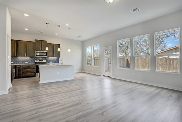 kitchen with light hardwood / wood-style flooring, an island with sink, stainless steel appliances, pendant lighting, and tasteful backsplash