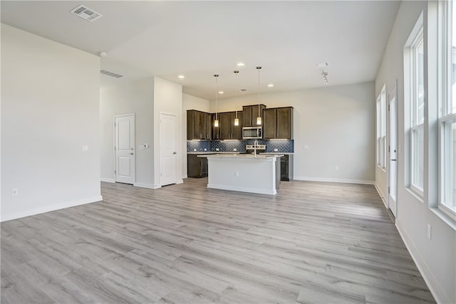 kitchen featuring a kitchen island with sink, light hardwood / wood-style flooring, pendant lighting, and tasteful backsplash