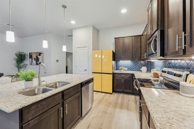 kitchen with pendant lighting, sink, light stone counters, stainless steel appliances, and a center island with sink