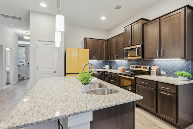 kitchen featuring sink, dark brown cabinets, appliances with stainless steel finishes, an island with sink, and light stone countertops