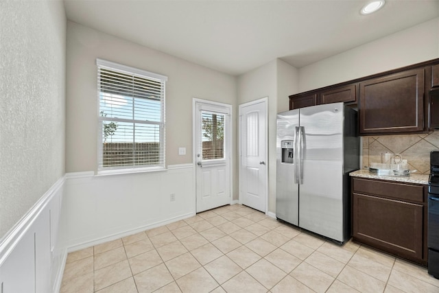 kitchen with wainscoting, light stone countertops, dark brown cabinetry, and stainless steel fridge with ice dispenser