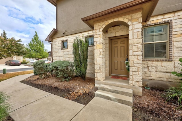 view of exterior entry featuring stone siding and stucco siding