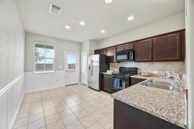 kitchen featuring a wainscoted wall, a sink, visible vents, light stone countertops, and black appliances