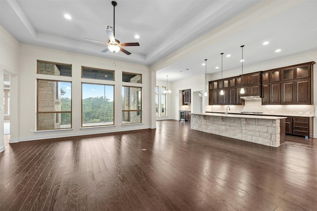 unfurnished living room featuring dark hardwood / wood-style floors, sink, a tray ceiling, and ceiling fan with notable chandelier