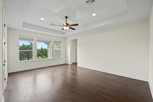 spare room with dark hardwood / wood-style floors, a tray ceiling, and ceiling fan