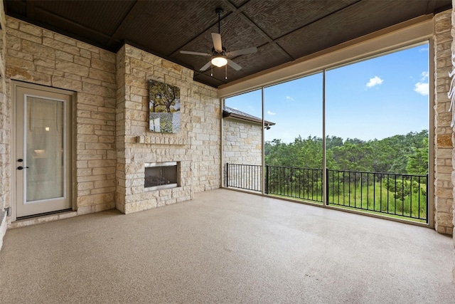 unfurnished sunroom featuring wood ceiling, an outdoor stone fireplace, and ceiling fan