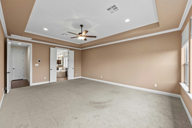 unfurnished bedroom with ornamental molding, ensuite bathroom, a tray ceiling, and carpet