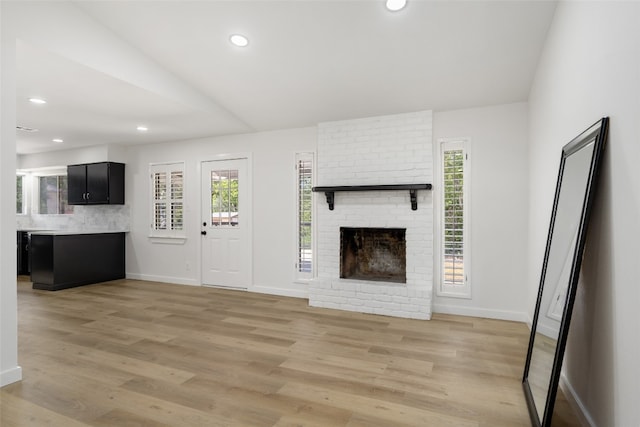 unfurnished living room featuring light hardwood / wood-style flooring and a brick fireplace