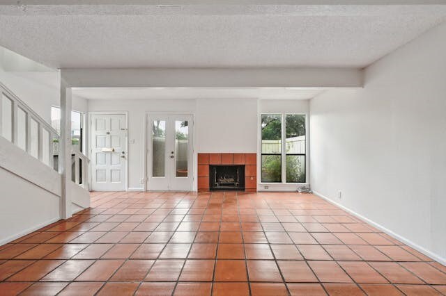 unfurnished living room featuring beam ceiling, a textured ceiling, and light tile patterned floors