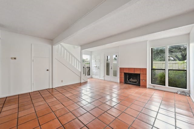 unfurnished living room featuring light tile patterned floors, beam ceiling, stairway, and a tiled fireplace