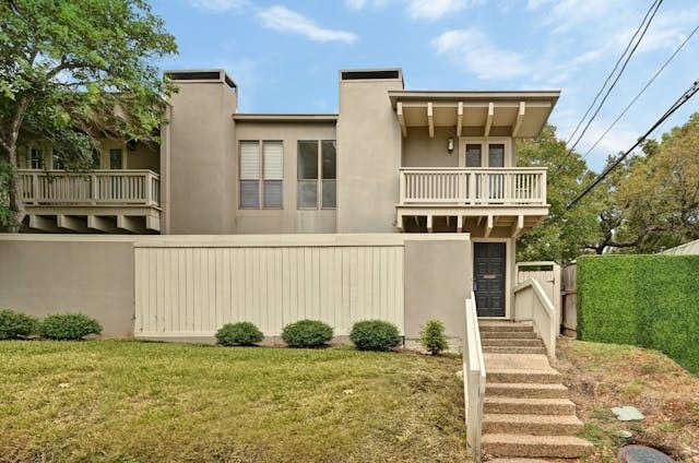 view of front of property with a fenced front yard, a balcony, a gate, stucco siding, and a front lawn