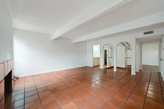 tiled empty room featuring beam ceiling and a fireplace