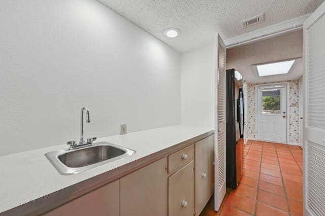 kitchen featuring a skylight, sink, a textured ceiling, tile patterned floors, and black refrigerator