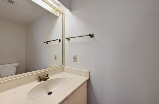 half bathroom featuring visible vents, vanity, and toilet