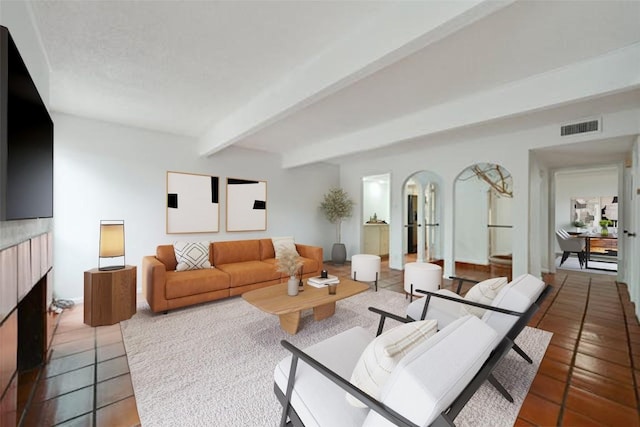 tiled living room with visible vents, beamed ceiling, and a fireplace