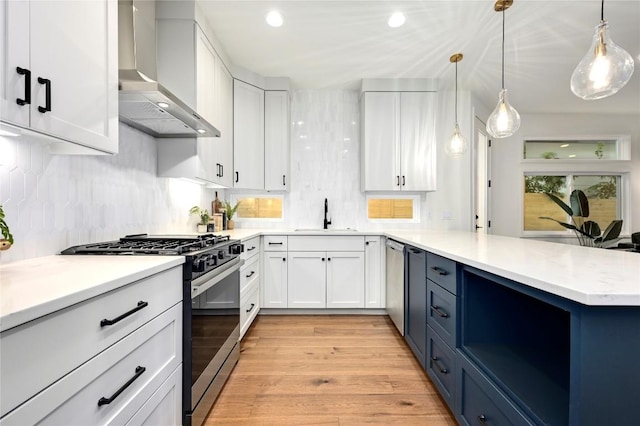 kitchen with white cabinets, sink, wall chimney exhaust hood, appliances with stainless steel finishes, and decorative light fixtures