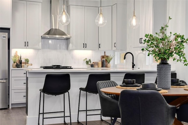 kitchen with hardwood / wood-style floors, white cabinetry, stainless steel refrigerator, and wall chimney exhaust hood