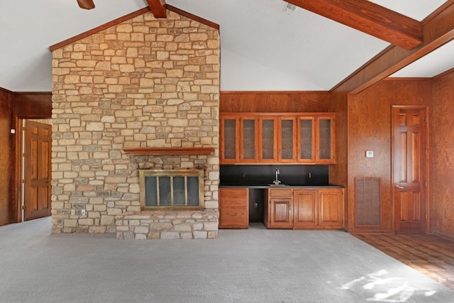 unfurnished living room with wooden walls, vaulted ceiling with beams, and light carpet