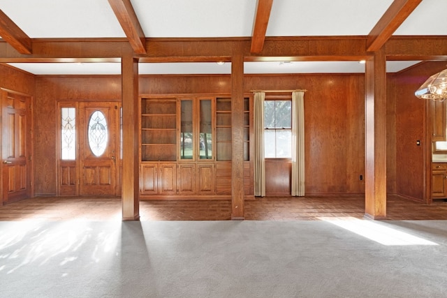 unfurnished living room featuring beam ceiling, wooden walls, and a healthy amount of sunlight