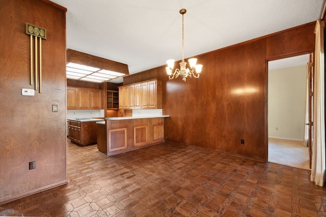 kitchen with kitchen peninsula, a textured ceiling, a chandelier, pendant lighting, and wooden walls