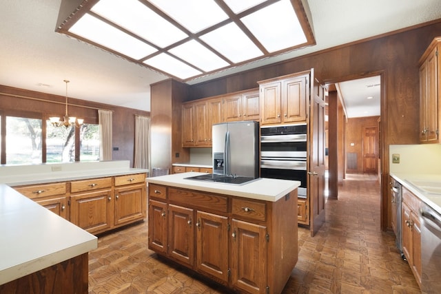 kitchen with appliances with stainless steel finishes, a chandelier, wood walls, pendant lighting, and a center island