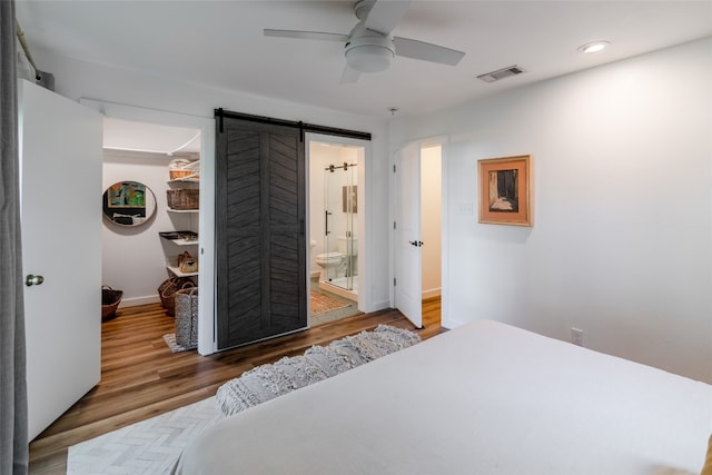 bedroom featuring connected bathroom, ceiling fan, hardwood / wood-style flooring, and a barn door