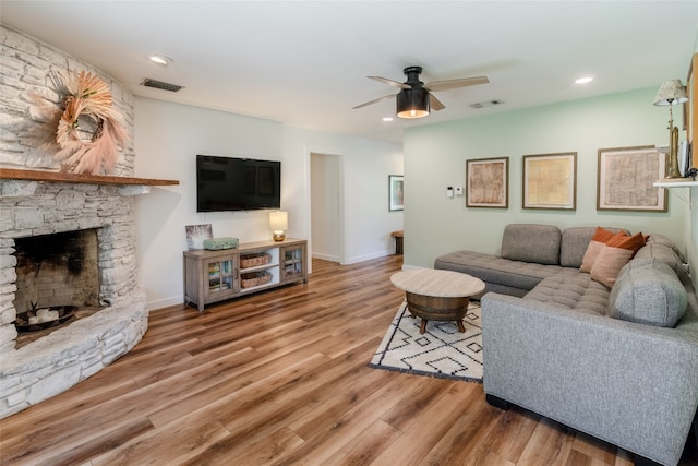 living room featuring ceiling fan, hardwood / wood-style flooring, and a stone fireplace