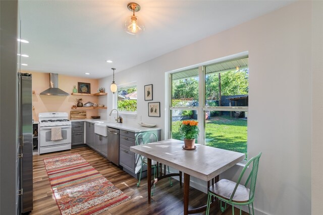 kitchen with wall chimney exhaust hood, gray cabinetry, sink, appliances with stainless steel finishes, and dark hardwood / wood-style flooring