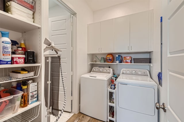 clothes washing area with cabinets, light hardwood / wood-style flooring, and washer and clothes dryer