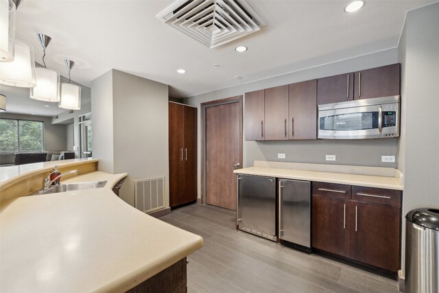 kitchen with dark brown cabinets, hanging light fixtures, sink, light hardwood / wood-style floors, and stainless steel appliances