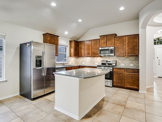 kitchen featuring appliances with stainless steel finishes, sink, a center island, lofted ceiling, and dark stone counters