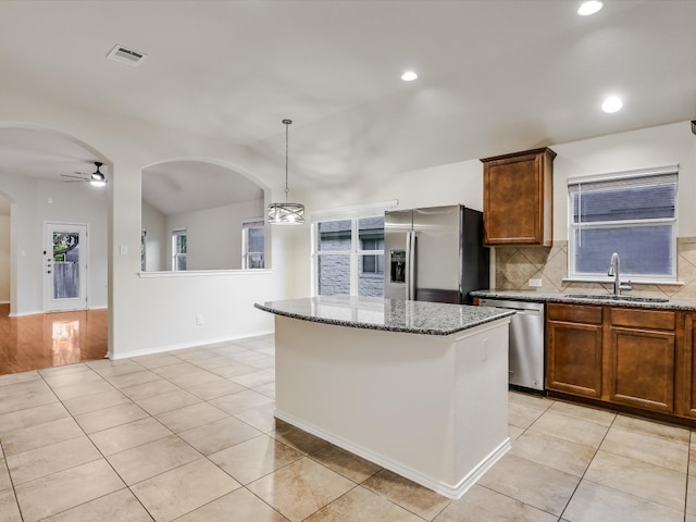 kitchen featuring hanging light fixtures, appliances with stainless steel finishes, sink, stone counters, and a center island