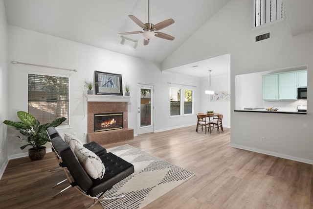 living room with high vaulted ceiling, ceiling fan, a premium fireplace, and light hardwood / wood-style floors