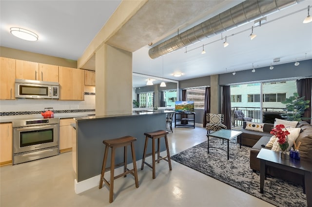 kitchen with plenty of natural light, appliances with stainless steel finishes, decorative light fixtures, and light brown cabinets