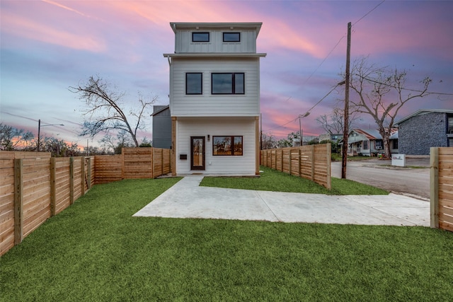 back house at dusk featuring a lawn and a patio