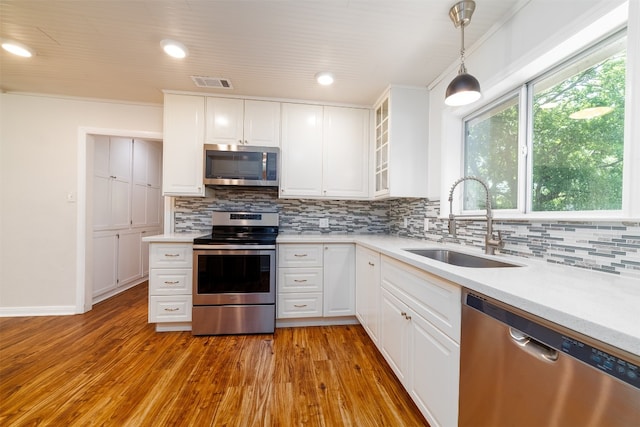 kitchen with hanging light fixtures, sink, white cabinets, light wood-type flooring, and appliances with stainless steel finishes