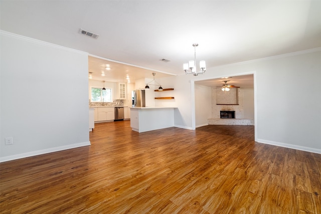 unfurnished living room with ceiling fan with notable chandelier, crown molding, a fireplace, and hardwood / wood-style floors