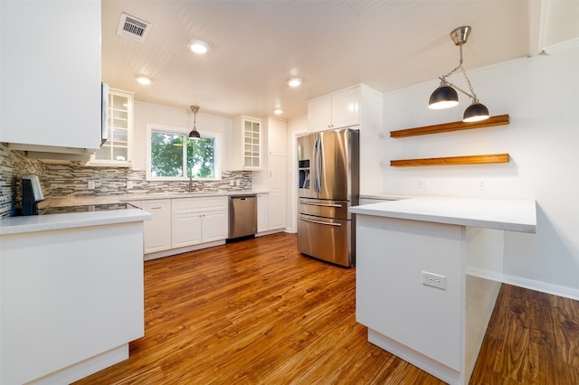 kitchen with kitchen peninsula, white cabinets, appliances with stainless steel finishes, hardwood / wood-style flooring, and pendant lighting