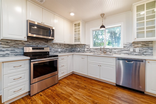 kitchen featuring sink, decorative light fixtures, white cabinetry, appliances with stainless steel finishes, and light hardwood / wood-style floors