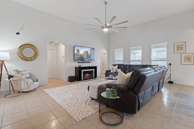 1336 Twin Estates Dr, Kyle, TX 78640 - living room featuring arched walkways, light tile patterned flooring, ceiling fan, a lit fireplace, and vaulted ceiling