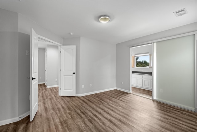 unfurnished bedroom featuring ensuite bathroom and hardwood / wood-style flooring